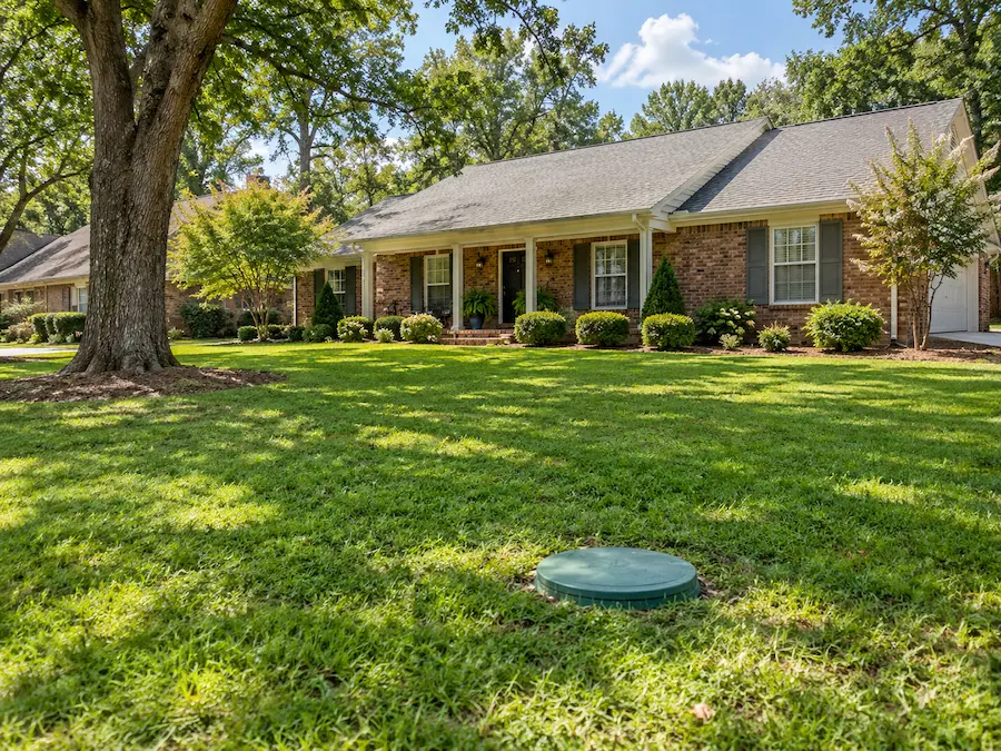 Brick ranch house in Huntsville, AL with a green septic tank riser lid in the front lawn